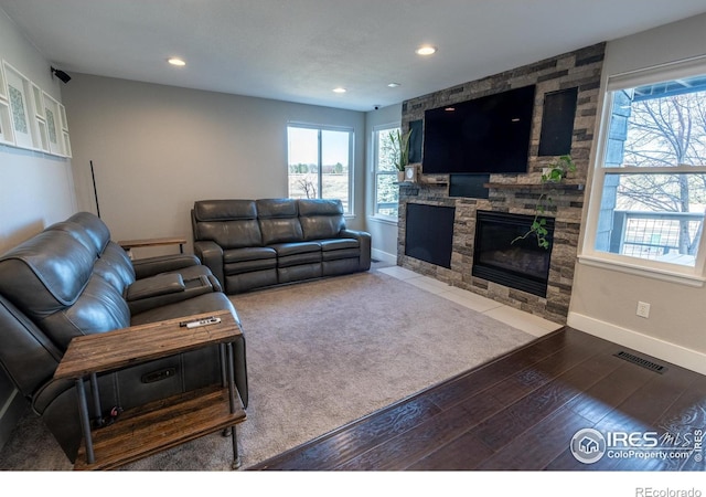 living room featuring visible vents, baseboards, hardwood / wood-style floors, a stone fireplace, and recessed lighting