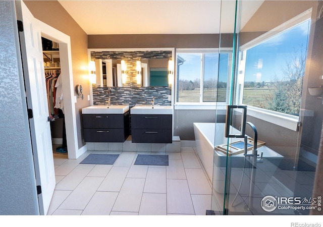 full bathroom featuring a spacious closet, decorative backsplash, two vanities, and a sink