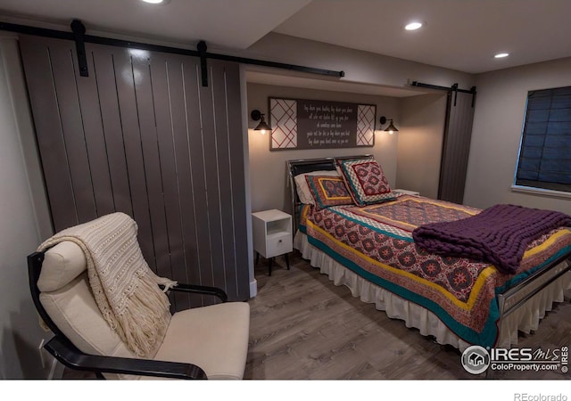 bedroom with recessed lighting, a barn door, and wood finished floors