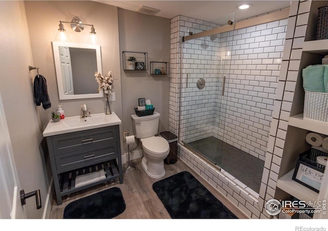 bathroom with a shower stall, baseboards, toilet, wood finished floors, and vanity