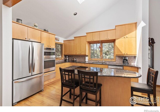82 Grove Ct, Boulder, CO 80302 - kitchen featuring stainless steel appliances, a sink, a kitchen breakfast bar, light brown cabinetry, and high vaulted ceiling