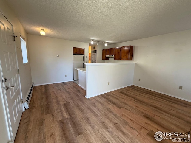 kitchen featuring under cabinet range hood, wood finished floors, freestanding refrigerator, a peninsula, and a baseboard radiator