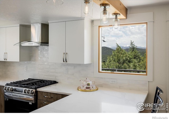 kitchen with light stone counters, stainless steel range with gas cooktop, white cabinets, wall chimney range hood, and tasteful backsplash