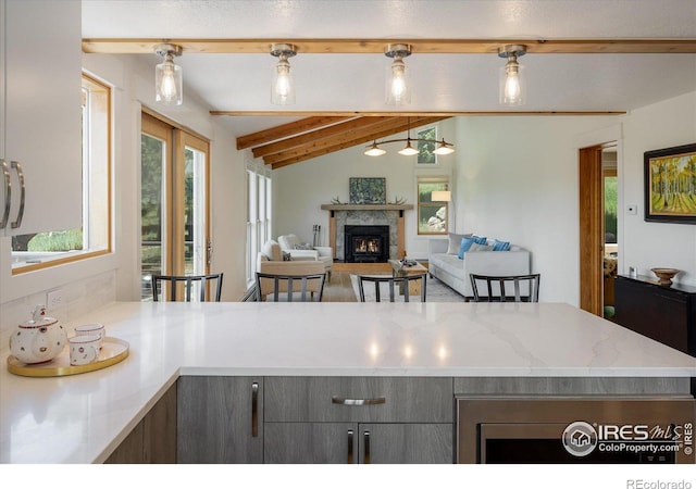 kitchen with lofted ceiling with beams, a healthy amount of sunlight, gray cabinets, and a warm lit fireplace