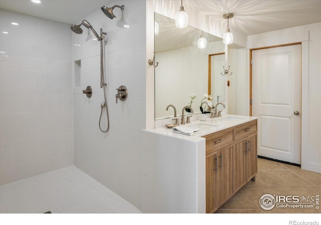 bathroom with a tile shower, tile patterned floors, double vanity, and a sink