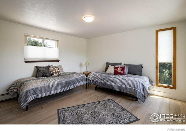 bedroom with a textured ceiling, wood finished floors, and a baseboard radiator