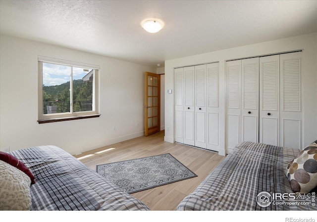 bedroom featuring light wood finished floors, a textured ceiling, baseboards, and multiple closets