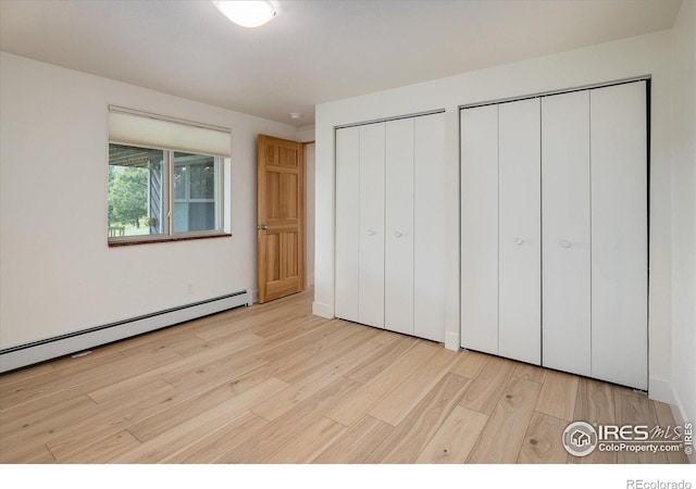 unfurnished bedroom with a baseboard radiator, multiple closets, and light wood-style floors