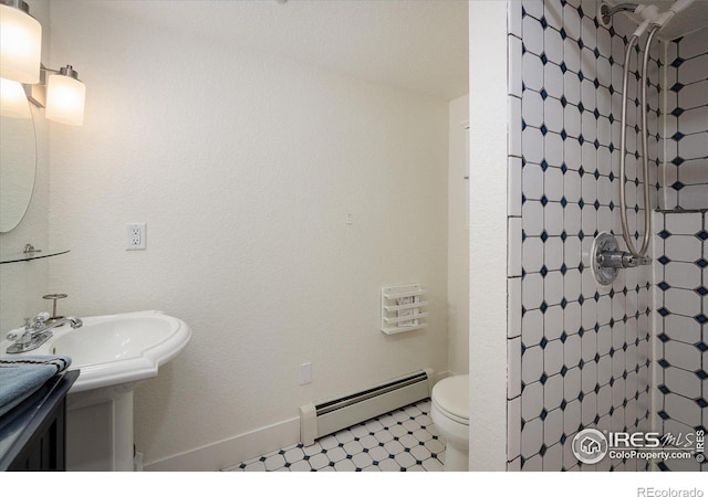 bathroom with a tile shower, baseboard heating, and toilet