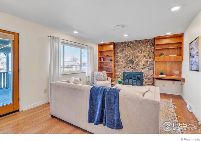 living area featuring built in features, a fireplace, light wood-style floors, and baseboards