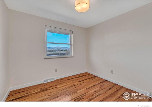 spare room featuring wood finished floors, visible vents, and baseboards