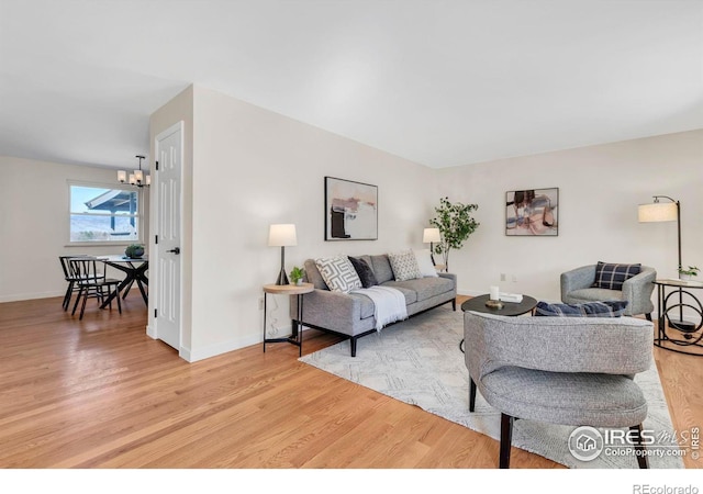 living area featuring light wood finished floors, a chandelier, and baseboards