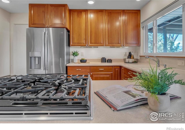 kitchen with brown cabinetry, gas range oven, stainless steel refrigerator with ice dispenser, and light countertops