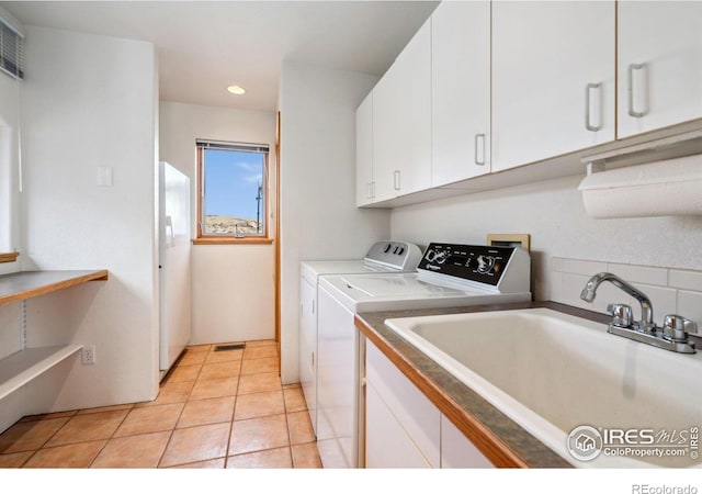 washroom with visible vents, a sink, cabinet space, light tile patterned floors, and washing machine and clothes dryer