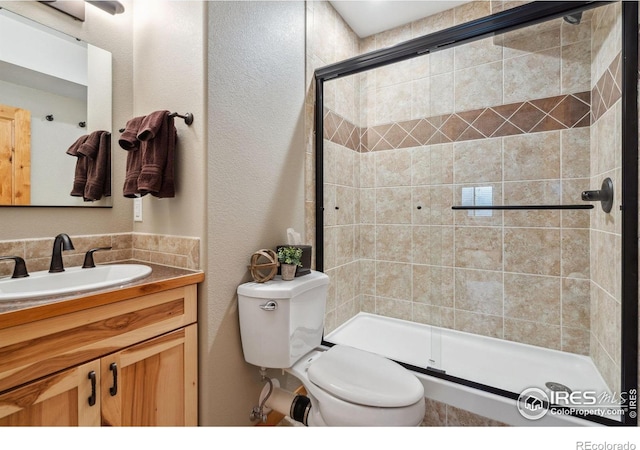 full bathroom with a shower stall, toilet, vanity, and a textured wall