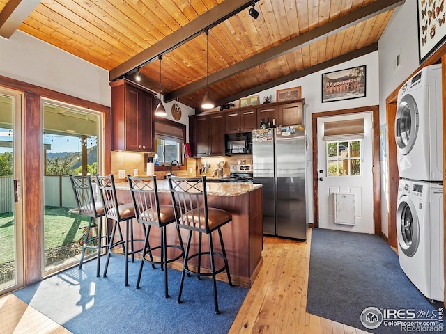 kitchen featuring vaulted ceiling with beams, a peninsula, wooden ceiling, stacked washing maching and dryer, and stainless steel appliances