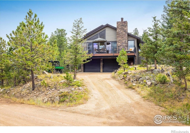 view of front of property featuring stone siding, a garage, driveway, and a chimney