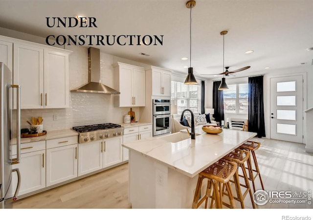 kitchen with tasteful backsplash, wall chimney range hood, a breakfast bar area, appliances with stainless steel finishes, and white cabinetry