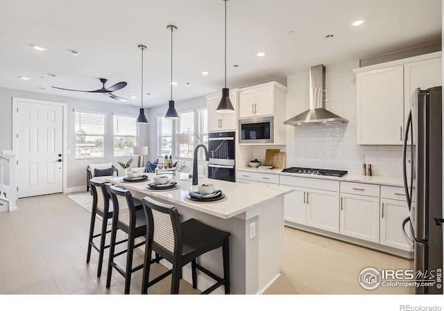 kitchen with backsplash, a breakfast bar, light countertops, stainless steel appliances, and wall chimney exhaust hood