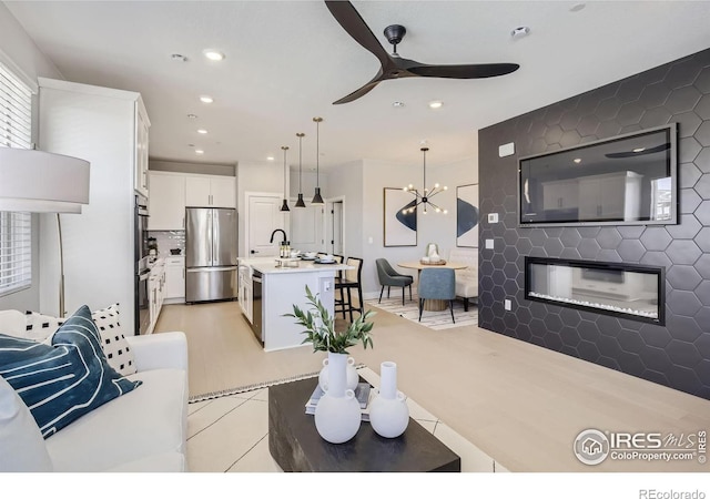 living area featuring recessed lighting, a glass covered fireplace, and ceiling fan with notable chandelier