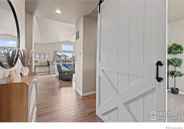 corridor with a barn door, lofted ceiling, baseboards, and wood finished floors