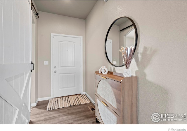 foyer entrance with a barn door, wood finished floors, baseboards, and visible vents