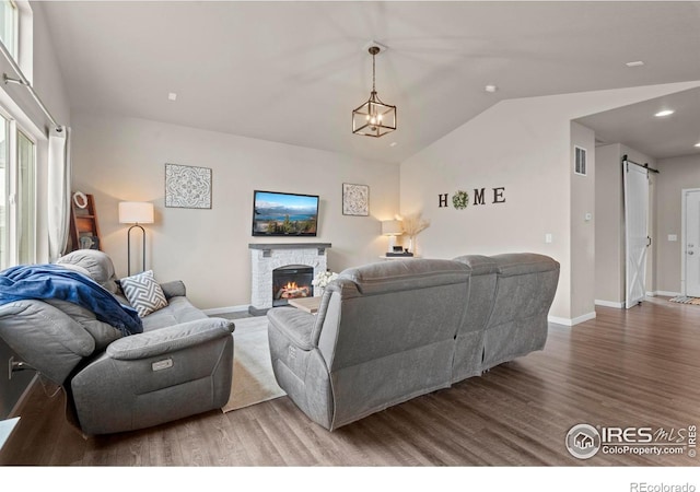 living area featuring visible vents, lofted ceiling, a barn door, a fireplace, and wood finished floors