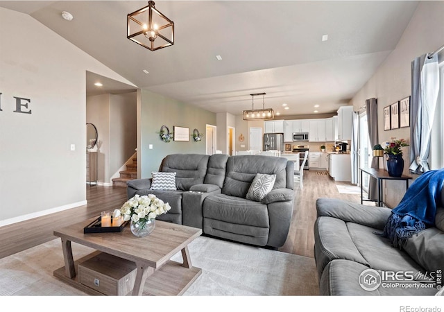 living area featuring stairway, baseboards, an inviting chandelier, lofted ceiling, and light wood-style floors