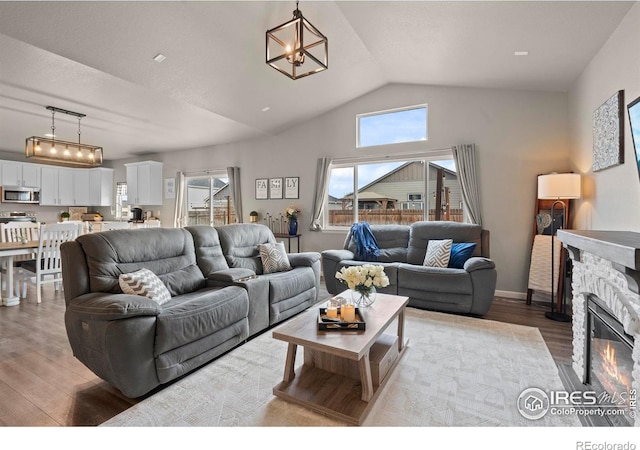 living area with wood finished floors, an inviting chandelier, a fireplace, baseboards, and vaulted ceiling