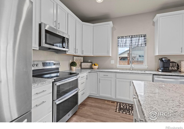 kitchen with a sink, stainless steel appliances, light wood-type flooring, and white cabinets