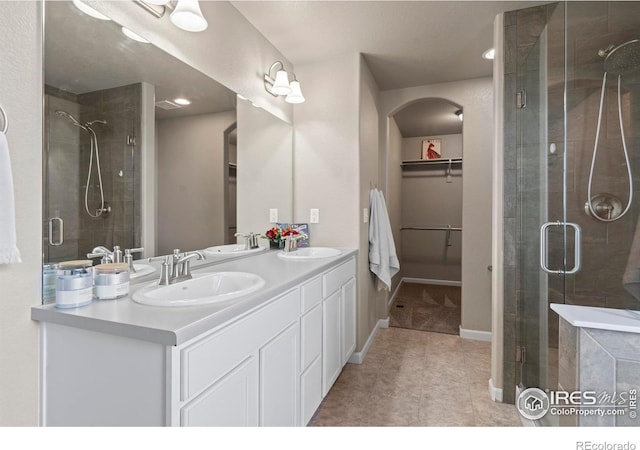 full bathroom with double vanity, a shower stall, a walk in closet, and a sink