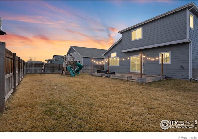 back of house at dusk featuring a patio area, a playground, a yard, and a fenced backyard