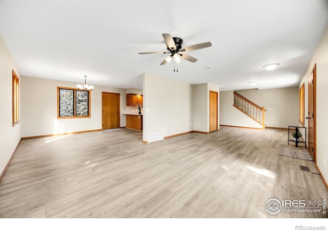 unfurnished living room featuring stairway, ceiling fan with notable chandelier, baseboards, and light wood finished floors