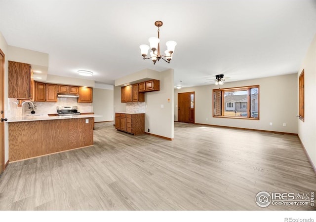 kitchen with a peninsula, stainless steel electric range oven, brown cabinetry, and under cabinet range hood