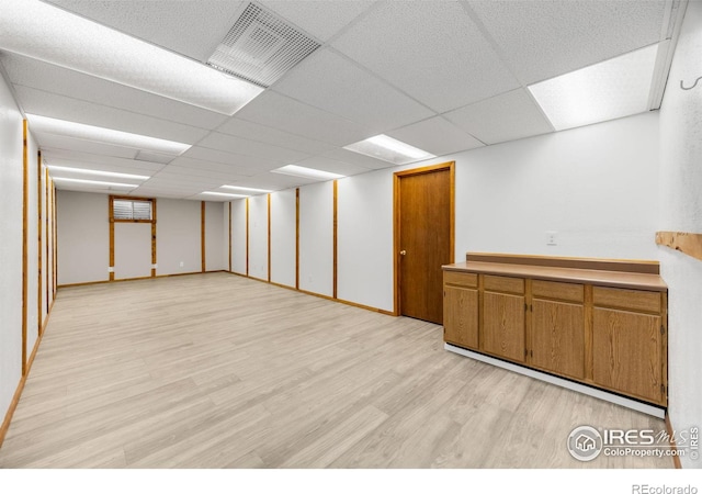 finished below grade area featuring a drop ceiling, visible vents, baseboards, and light wood-style floors