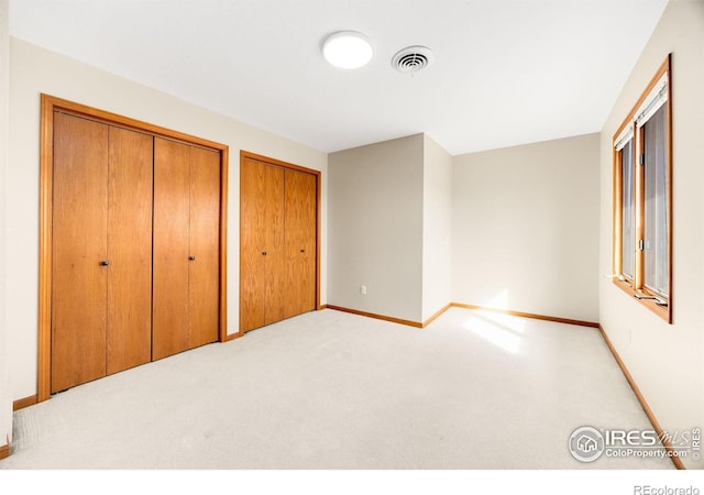 unfurnished bedroom featuring baseboards, carpet, visible vents, and multiple closets