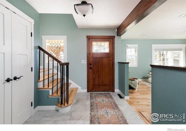 foyer entrance with beam ceiling, stairs, and baseboards