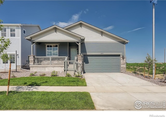 view of front facade featuring a porch, stone siding, a garage, and driveway