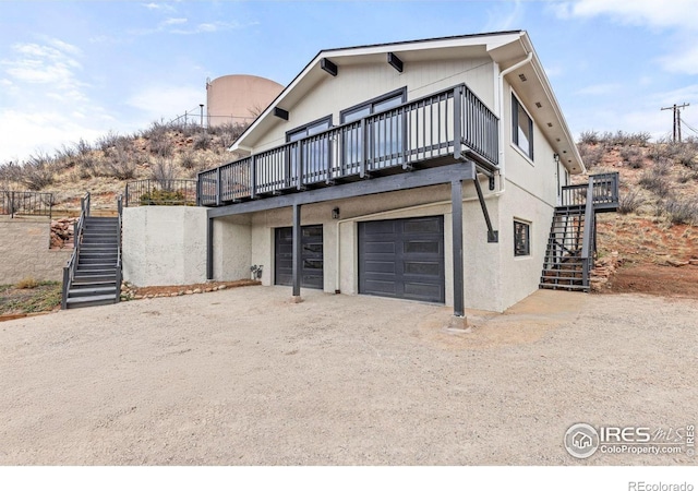 back of house with stairs, an attached garage, and driveway