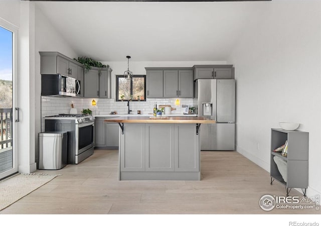 kitchen with tasteful backsplash, gray cabinetry, a center island, lofted ceiling, and appliances with stainless steel finishes