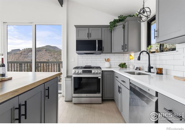 kitchen featuring tasteful backsplash, lofted ceiling, gray cabinets, stainless steel appliances, and a sink