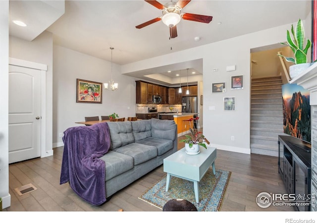 living area with visible vents, a raised ceiling, wood finished floors, baseboards, and stairs