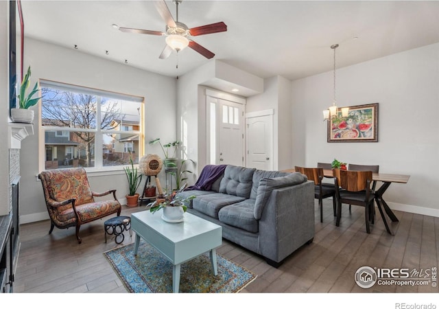 living area with plenty of natural light, ceiling fan with notable chandelier, baseboards, and wood-type flooring