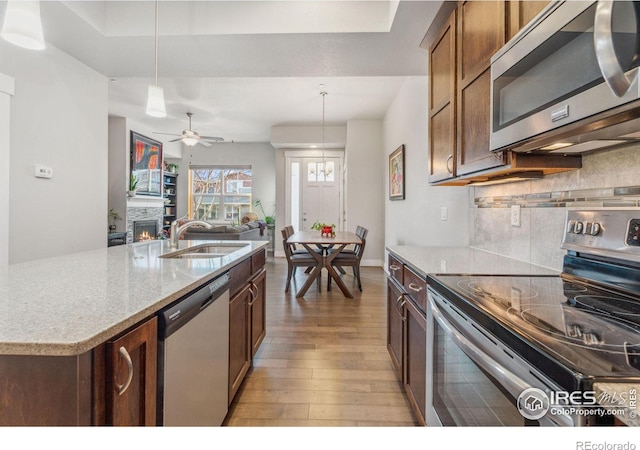 kitchen featuring light wood-style flooring, a sink, a lit fireplace, appliances with stainless steel finishes, and tasteful backsplash