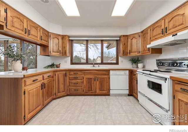 kitchen featuring under cabinet range hood, light countertops, brown cabinets, white appliances, and a sink