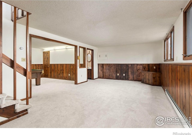 carpeted empty room featuring a textured ceiling, a wainscoted wall, baseboard heating, and wood walls