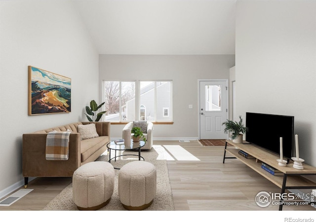 living area featuring baseboards, visible vents, light wood finished floors, and high vaulted ceiling