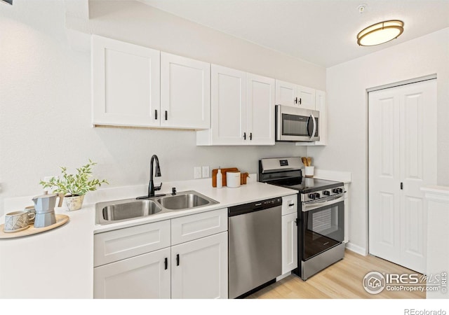 kitchen with a sink, light wood-style floors, appliances with stainless steel finishes, white cabinets, and light countertops