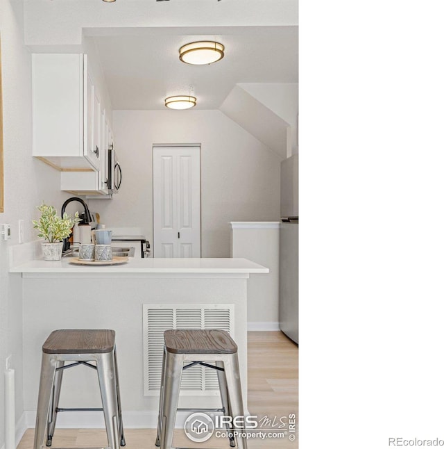 kitchen featuring a breakfast bar, light wood-type flooring, a peninsula, stainless steel appliances, and white cabinetry