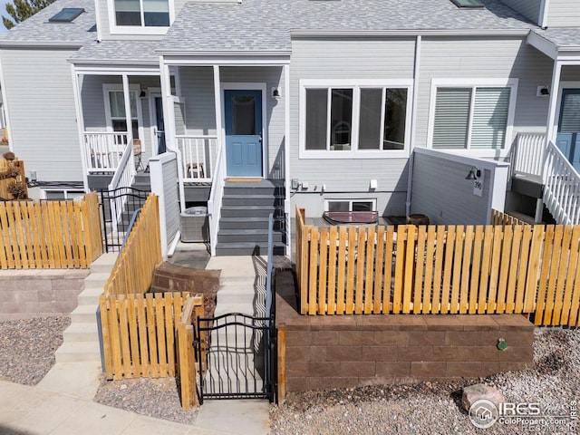 view of front facade featuring a porch, a shingled roof, stairs, and fence